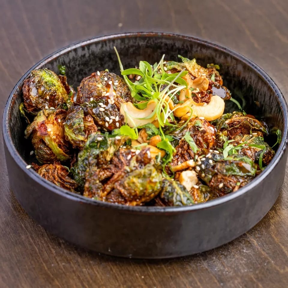 Roasted Brussels sprouts with cashews, sesame seeds, and microgreens in a dark bowl.