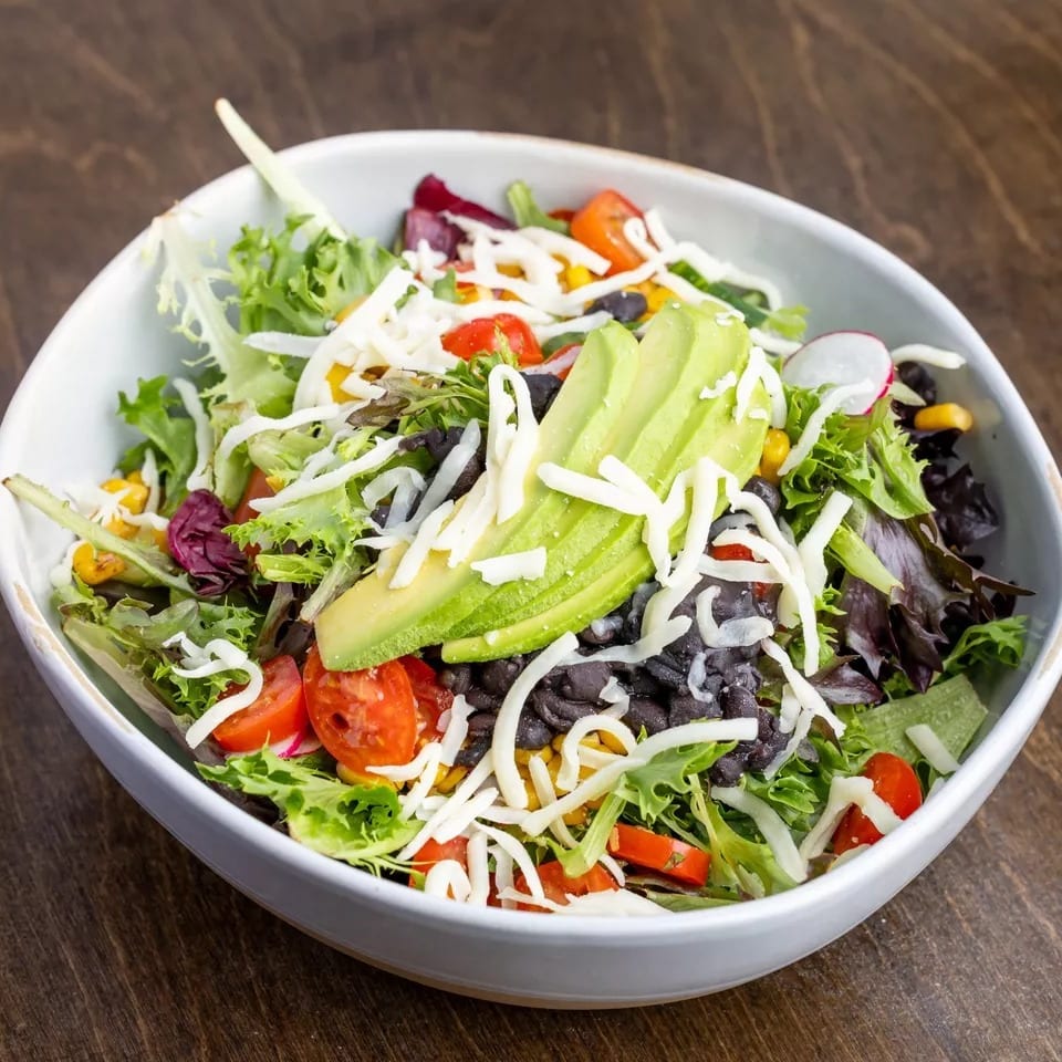 Fresh salad with mixed greens, black beans, corn, cherry tomatoes, avocado, and shredded cheese.