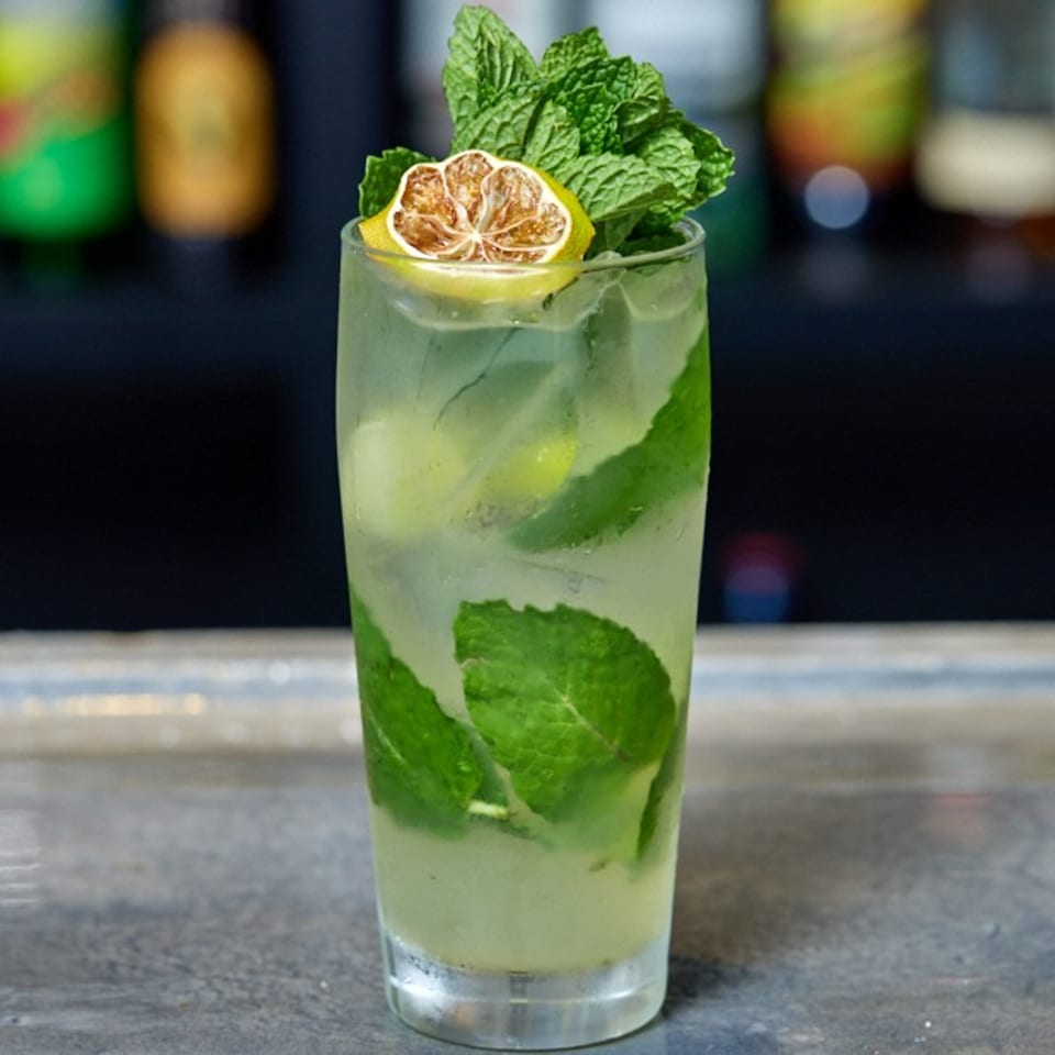 Refreshing mojito cocktail with mint leaves and a dried lime slice on a bar counter.
